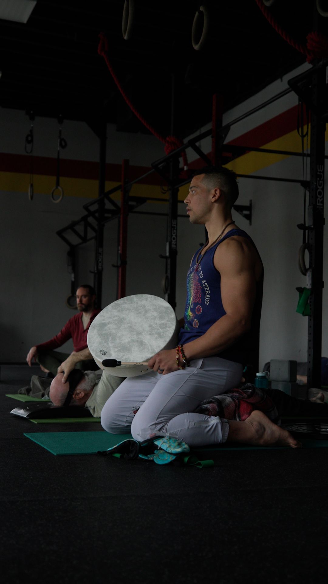 A man is kneeling down while holding a drum in a gym.