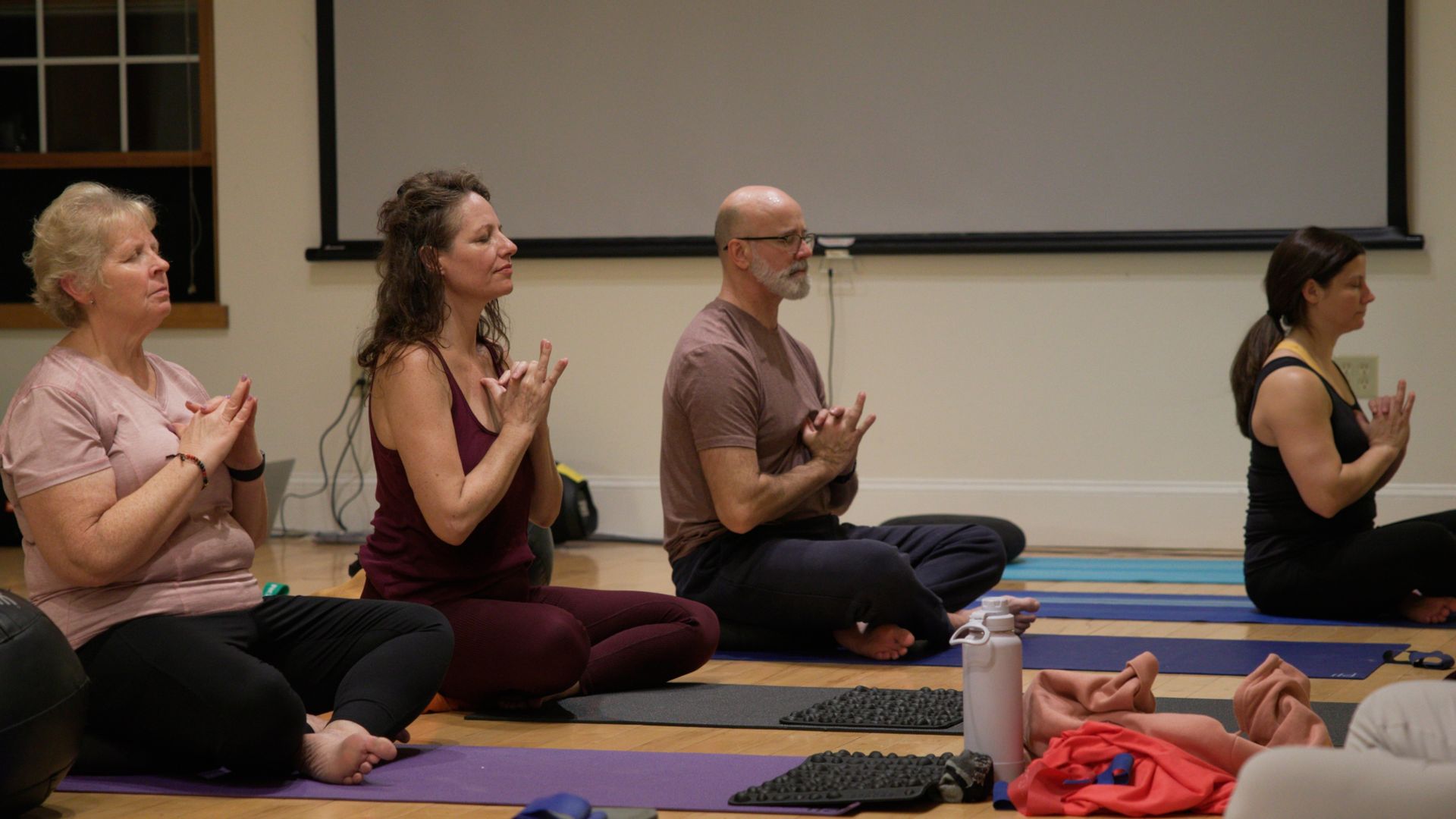 A group of people are sitting on yoga mats in a room.