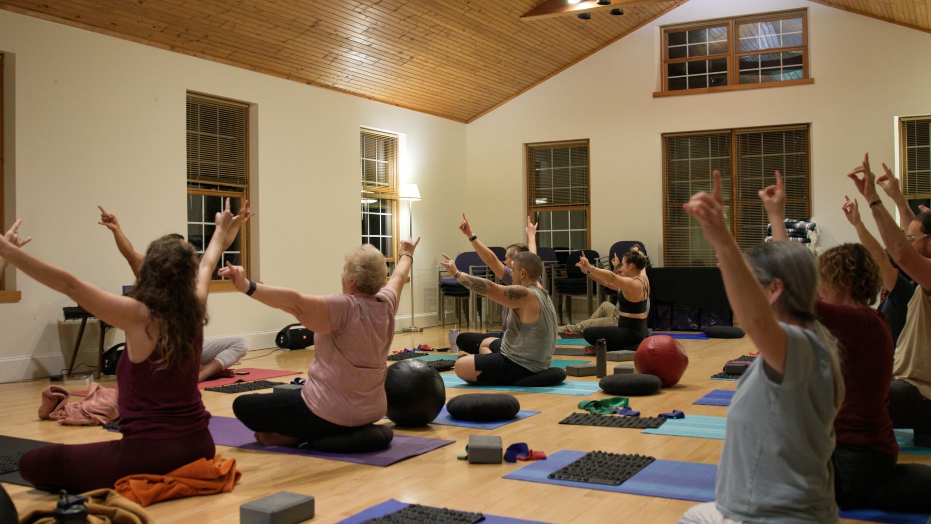 A group of people are doing yoga in a room with their arms in the air.