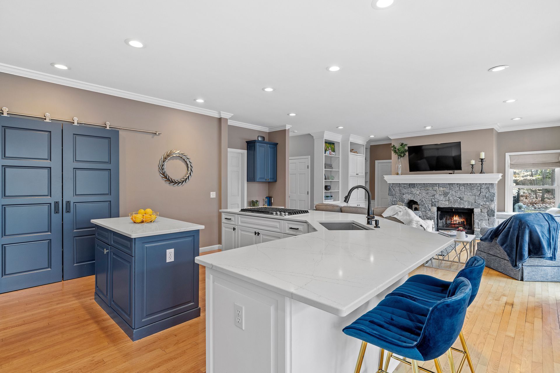 Kitchen with blue and white cabients and white quartz countertop. Fireplace with mantel, blue chairs and blue barn doors.