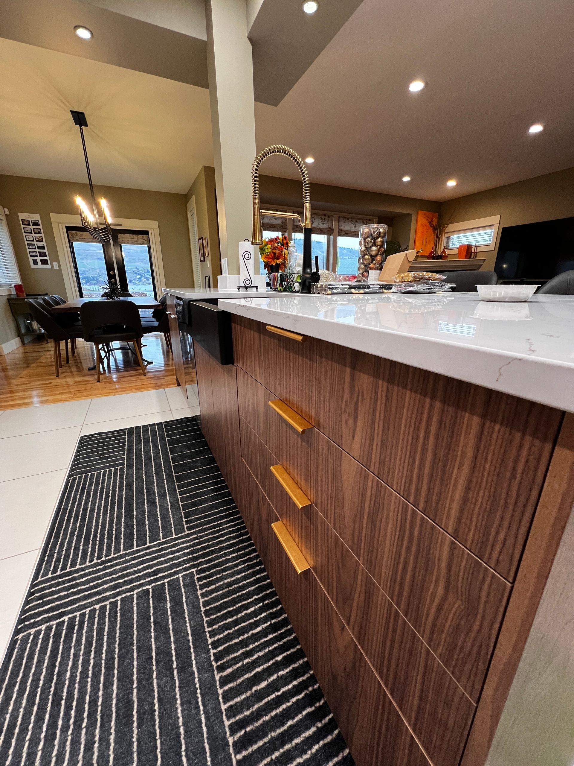 Brown wood cabinets with gold handles/hardware, white quartz countertop, white tiles and hardwood flooring