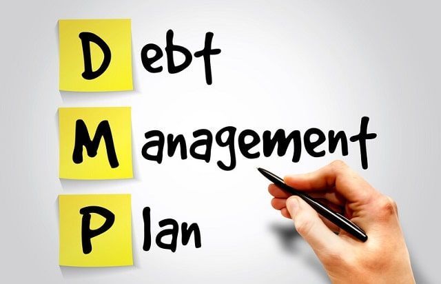 A person is writing the word debt management on a piece of paper