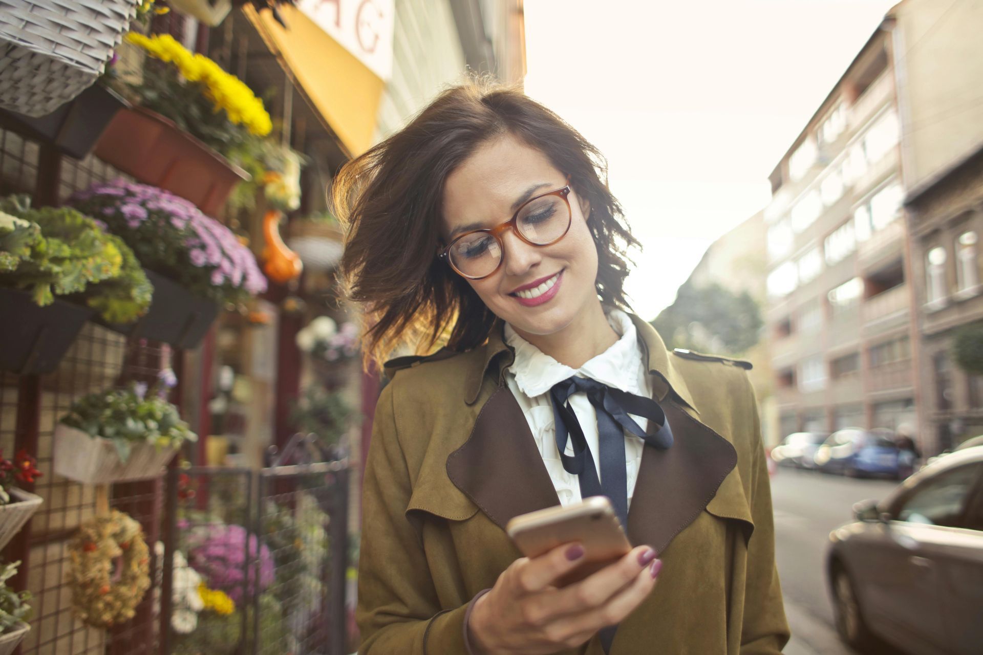 A woman is standing on a sidewalk looking at her cell phone.