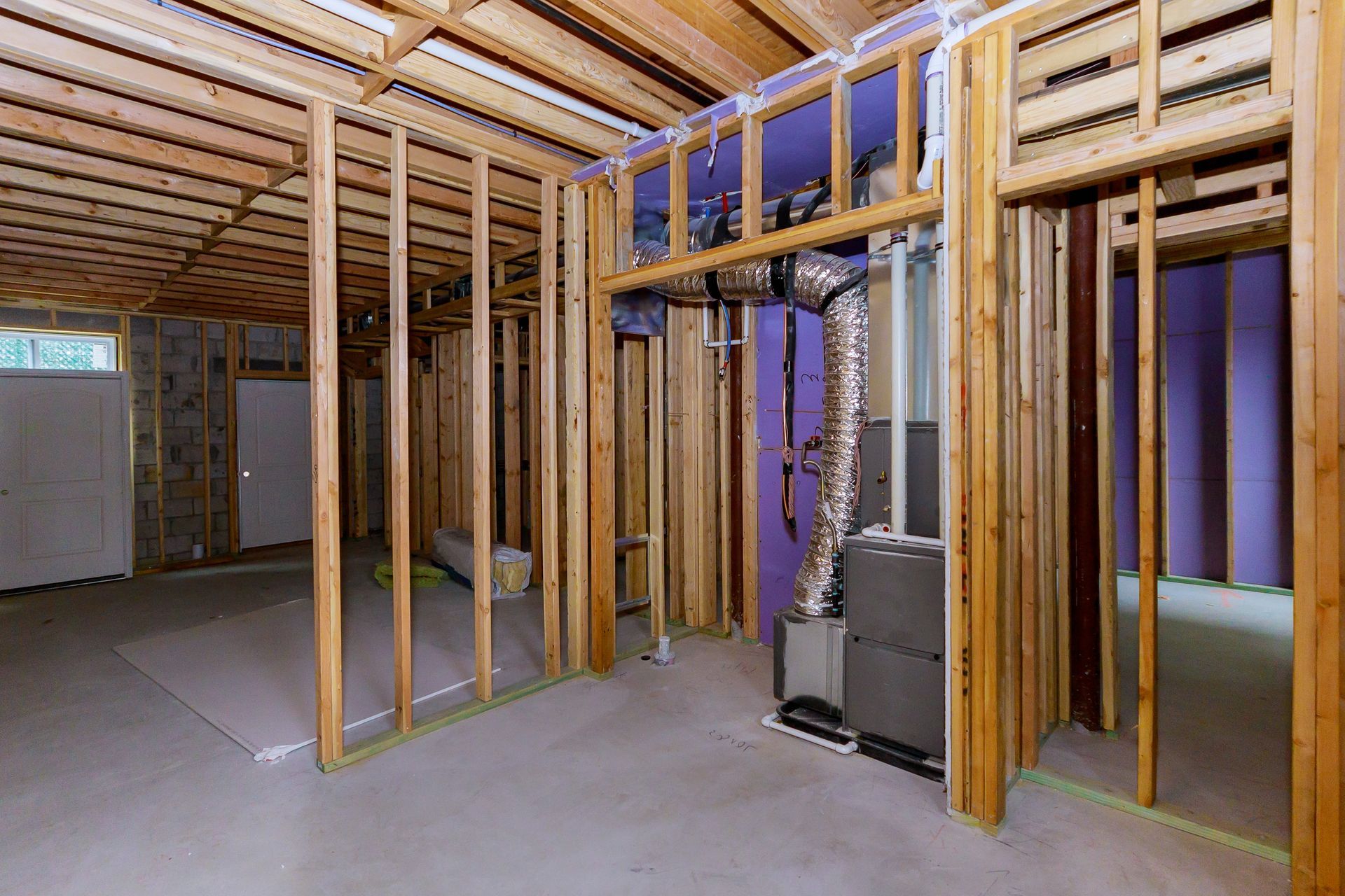 Interior view of a basement under construction, showing wooden framing, ductwork, and concrete flooring.