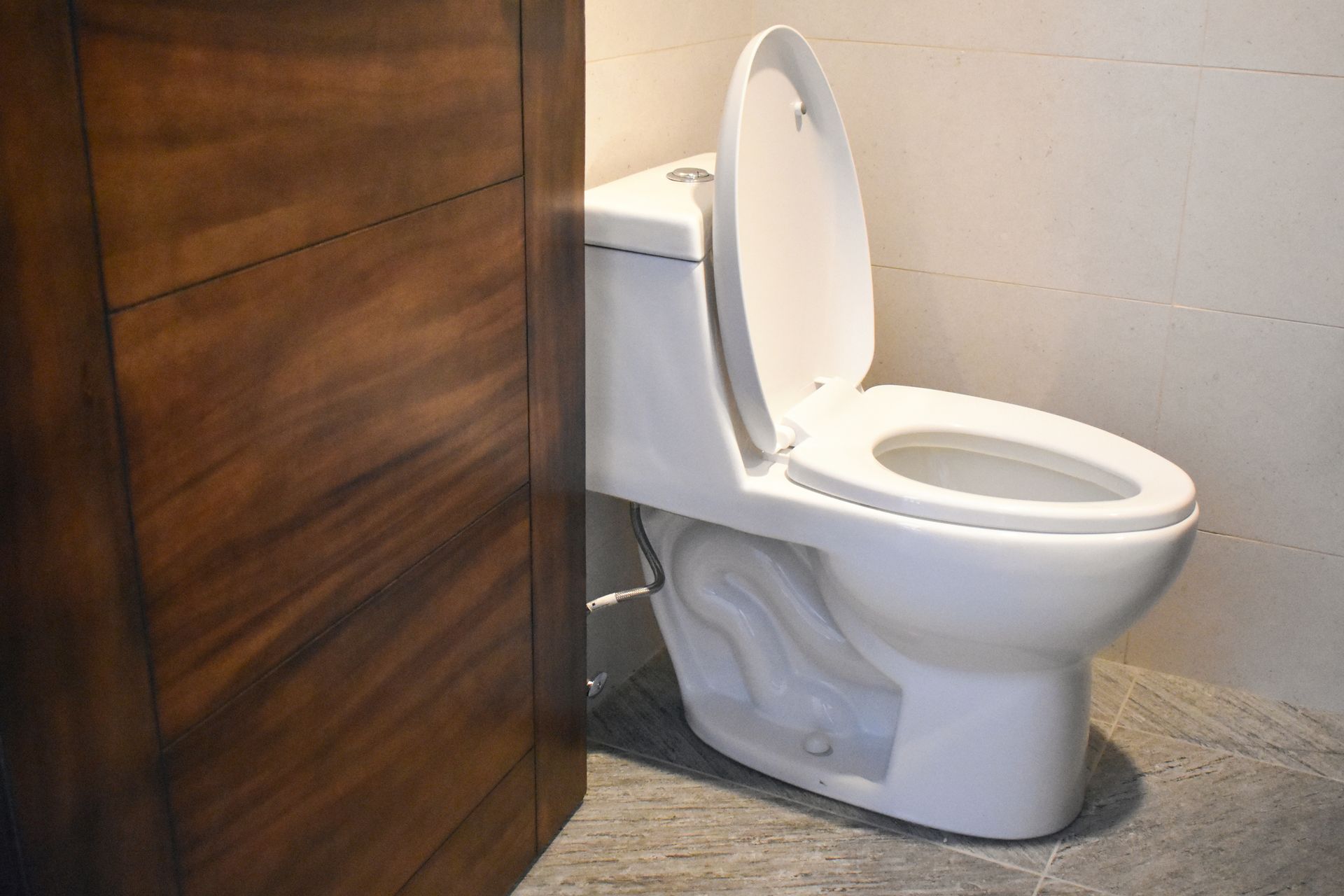 White toilet beside a wooden partition in a bathroom, with the seat and lid raised.