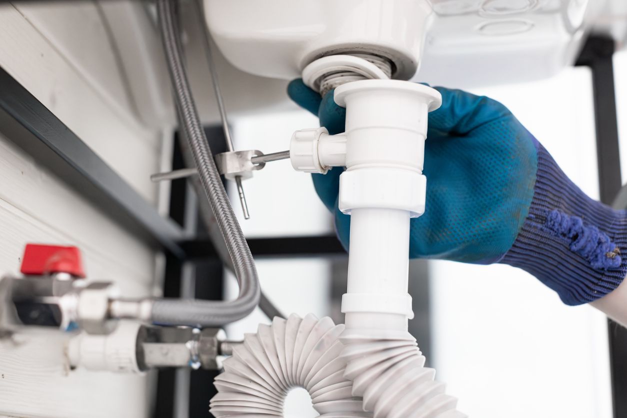 Hand using a wrench to tighten a white sink drain pipe under a bathroom sink