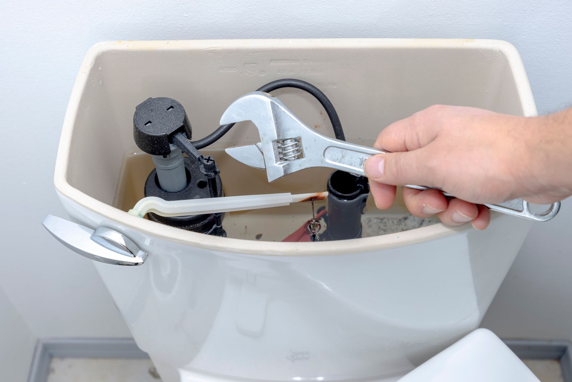 Person using a wrench to repair the inner workings of a toilet tank.