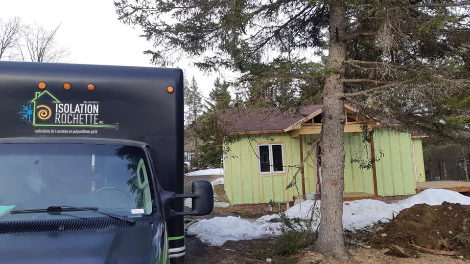 Camion noir avec le logo de l'entreprise stationné près d'une maison vert clair en construction, avec de la neige au sol.