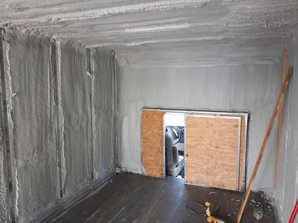 Intérieur d'un conteneur de fret isolé avec de la mousse pulvérisée grise, des portes en contreplaqué, un plancher foncé et deux poteaux.