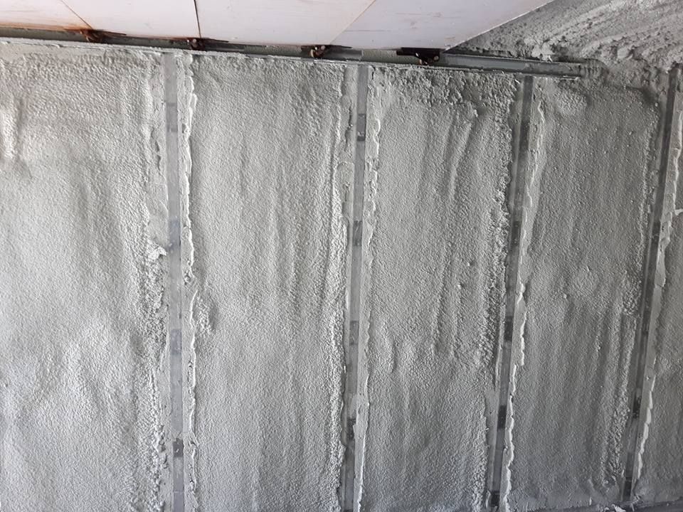 Mur avec montants métalliques recouverts d'une isolation en mousse pulvérisée texturée de couleur claire.