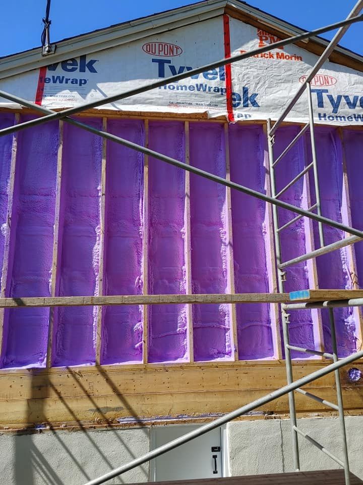 Mur en construction, rempli d'isolant violet, échafaudage devant, fond de ciel bleu.