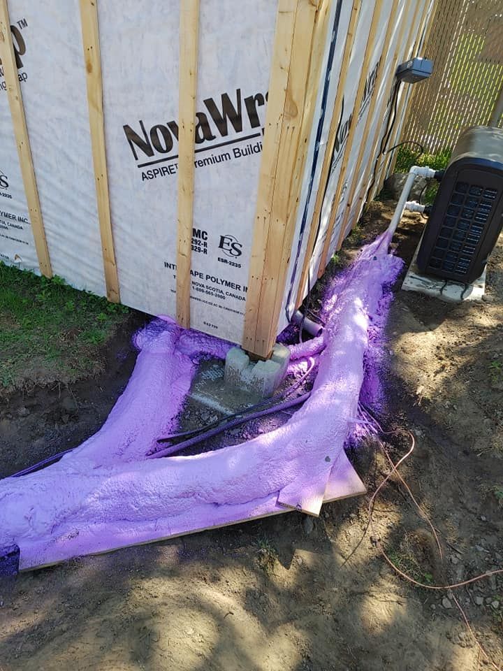 De la mousse isolante violette pulvérisée se répand depuis la base d'un bâtiment sur la terre, à côté d'une unité extérieure.