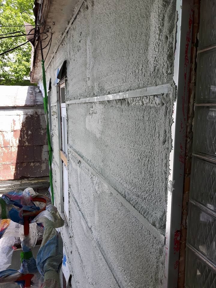 Mur extérieur en stuc frais. Des bandes métalliques et un cadre de fenêtre sont visibles.