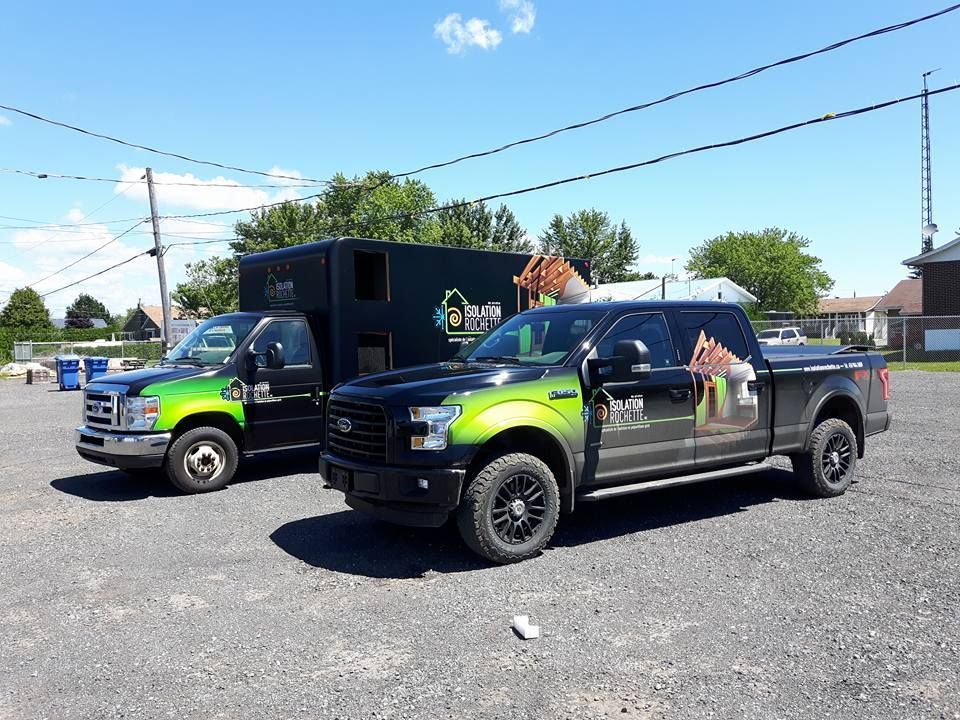Deux camions d'entreprise, noirs avec des accents verts, stationnés sur un terrain par une journée ensoleillée.