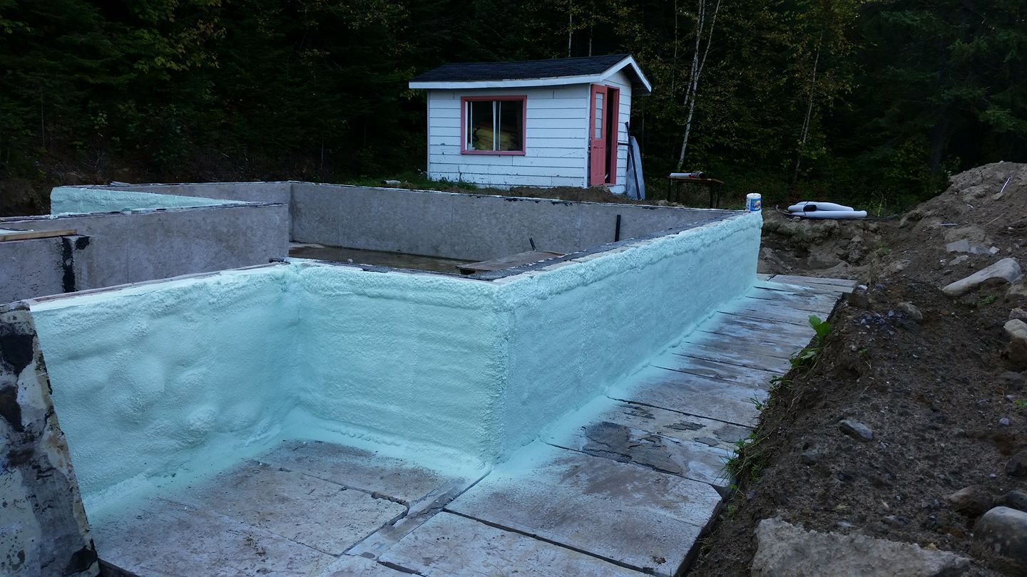 Murs de fondation avec isolation en mousse pulvérisée, avec un petit hangar en arrière-plan.