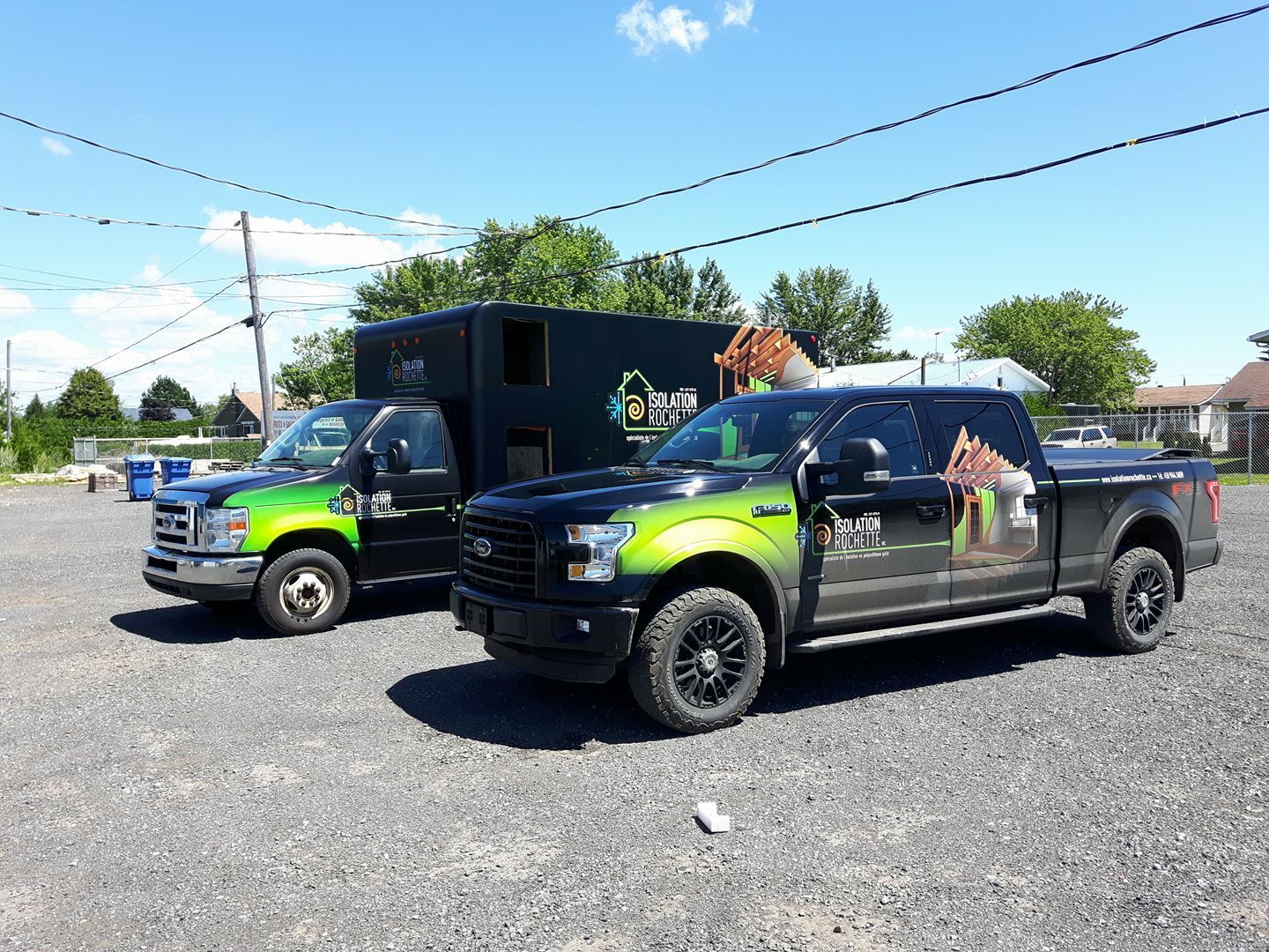 Deux camions de travail noirs avec des graphismes vert citron garés sur du gravier sous un ciel bleu.