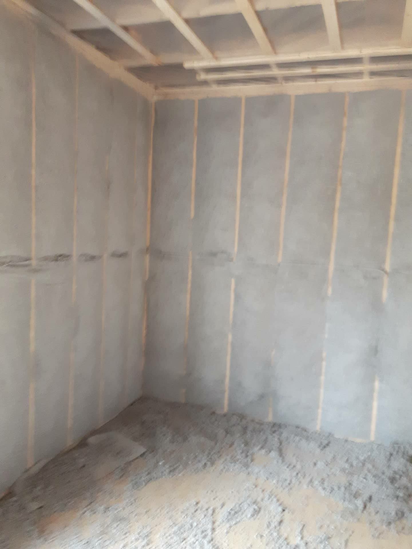 Pièce intérieure en construction, murs recouverts d'isolant gris, sol avec débris.