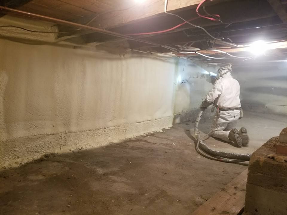 Une personne en combinaison de protection pulvérise de l'isolant sur le mur du sous-sol.