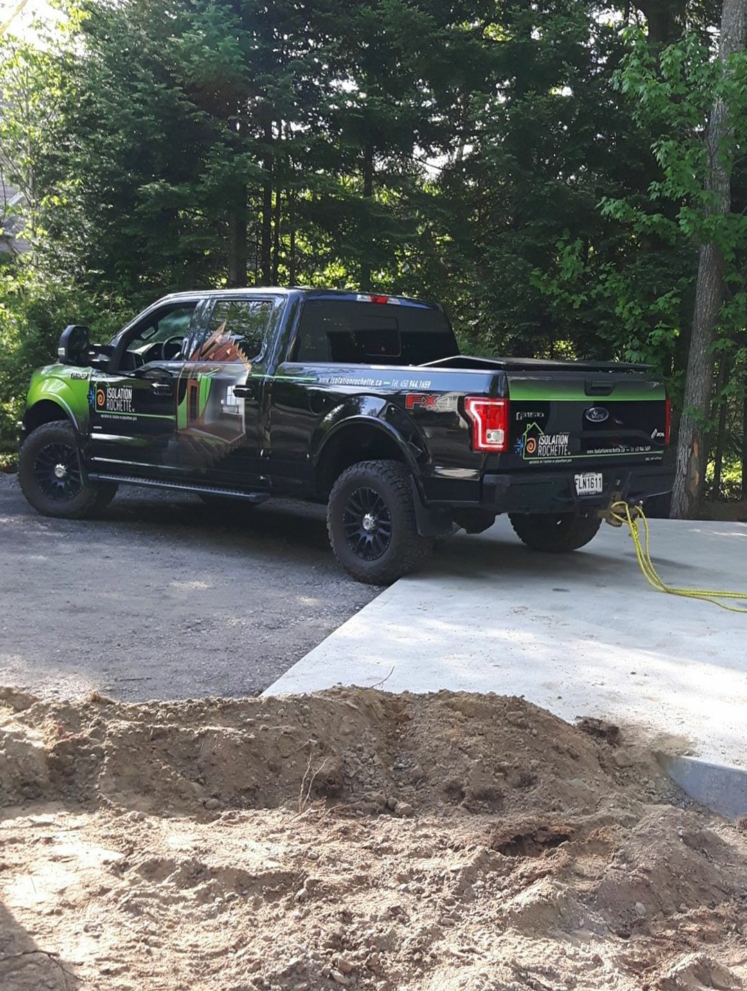 Pick-up noir aux touches de vert garé près d'une dalle de béton. Des arbres en arrière-plan.