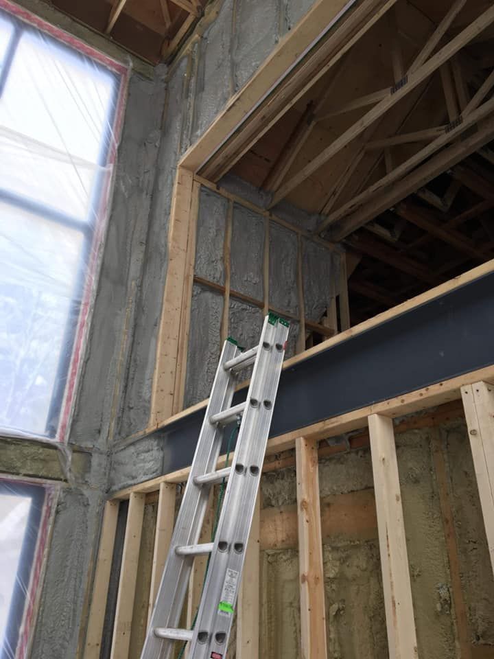 Échelle appuyée contre un bâtiment partiellement construit avec une grande fenêtre et des poutres apparentes.