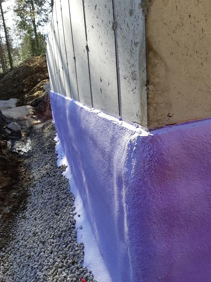 Isolation en mousse pulvérisée violette sur une fondation en béton, avec drainage de gravier le long du sol.