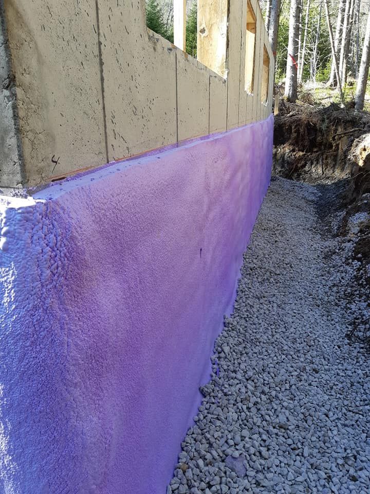 Mur de fondation avec isolation violette, gravier et structure en béton dans un cadre naturel.