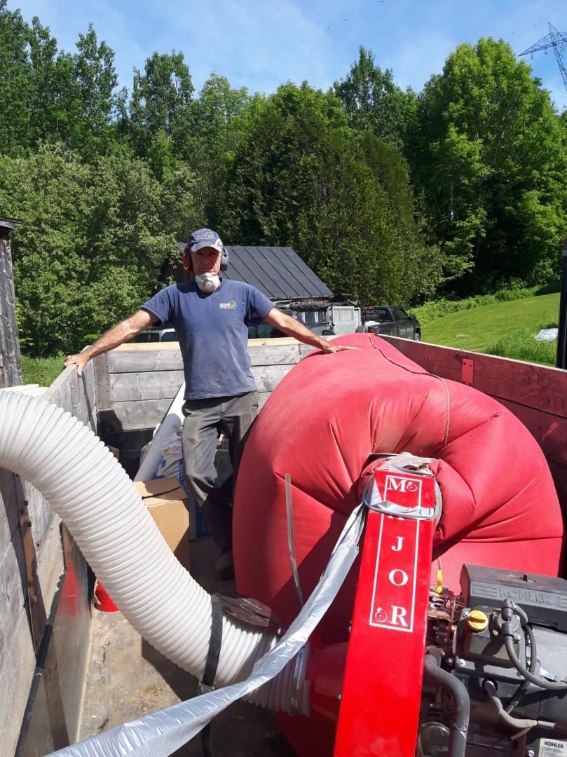 Une personne se tient debout dans la benne d'un camion, à côté d'un grand sac de rangement gonflable rouge relié à un tuyau et à une armature métallique rouge.