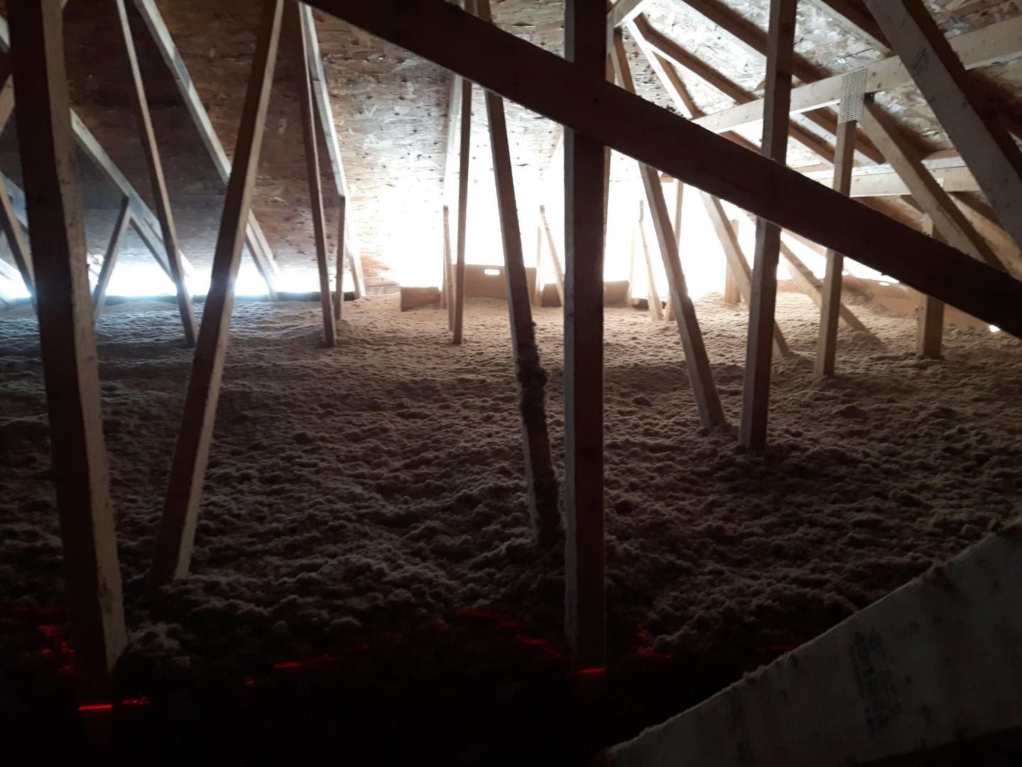 Un espace mansardé révélant une charpente de toit en bois avec un isolant en vrac recouvrant le sol.