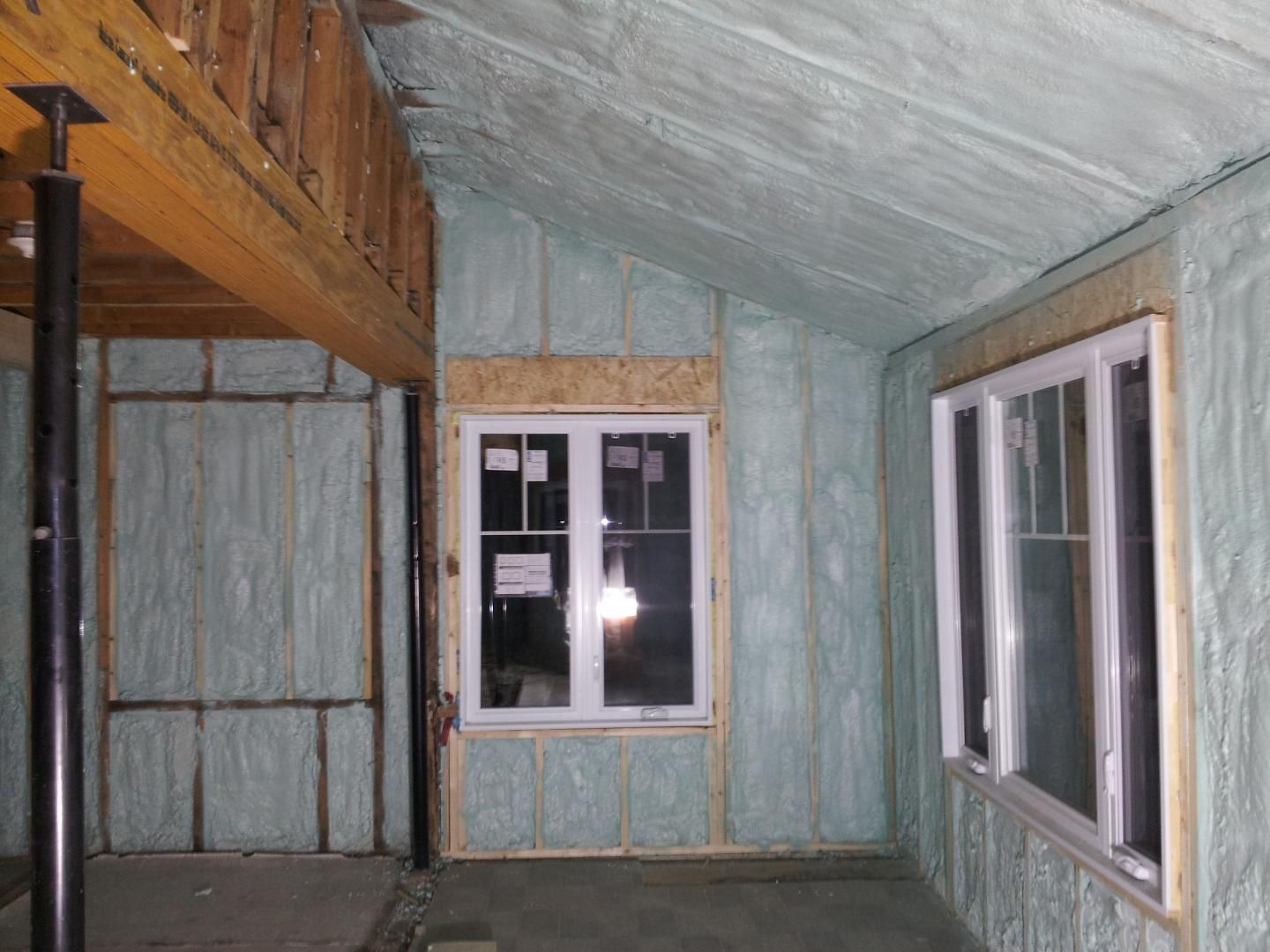 Vue intérieure d'une pièce en cours d'isolation par mousse expansive. Les murs et le plafond sont recouverts d'isolant vert clair. Deux fenêtres sont visibles.