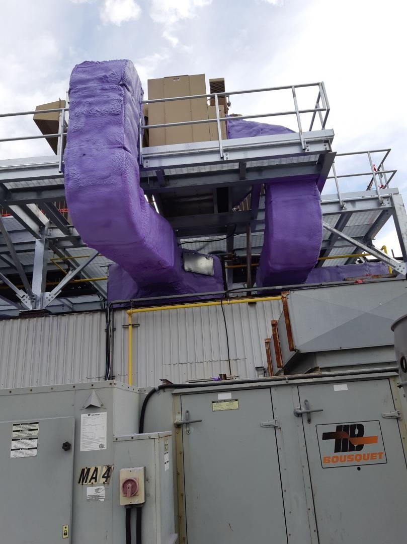 Conduits de CVC isolés en violet sur un toit, entourés d'une cage métallique. Des boîtiers sont posés dessus.