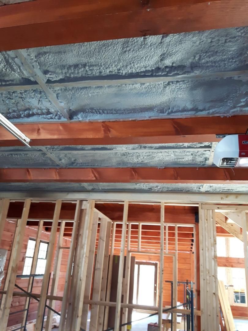 Vue intérieure d'un bâtiment en construction, montrant l'isolation en mousse projetée au plafond et la charpente en bois.