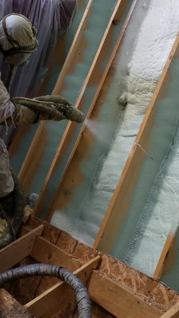 Une personne pulvérise de l'isolant en mousse entre les chevrons en bois d'un grenier.