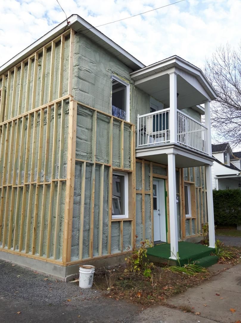 Maison en rénovation (extérieur) : charpente en bois installée, isolation vert clair visible. Balcon avec rambarde blanche.