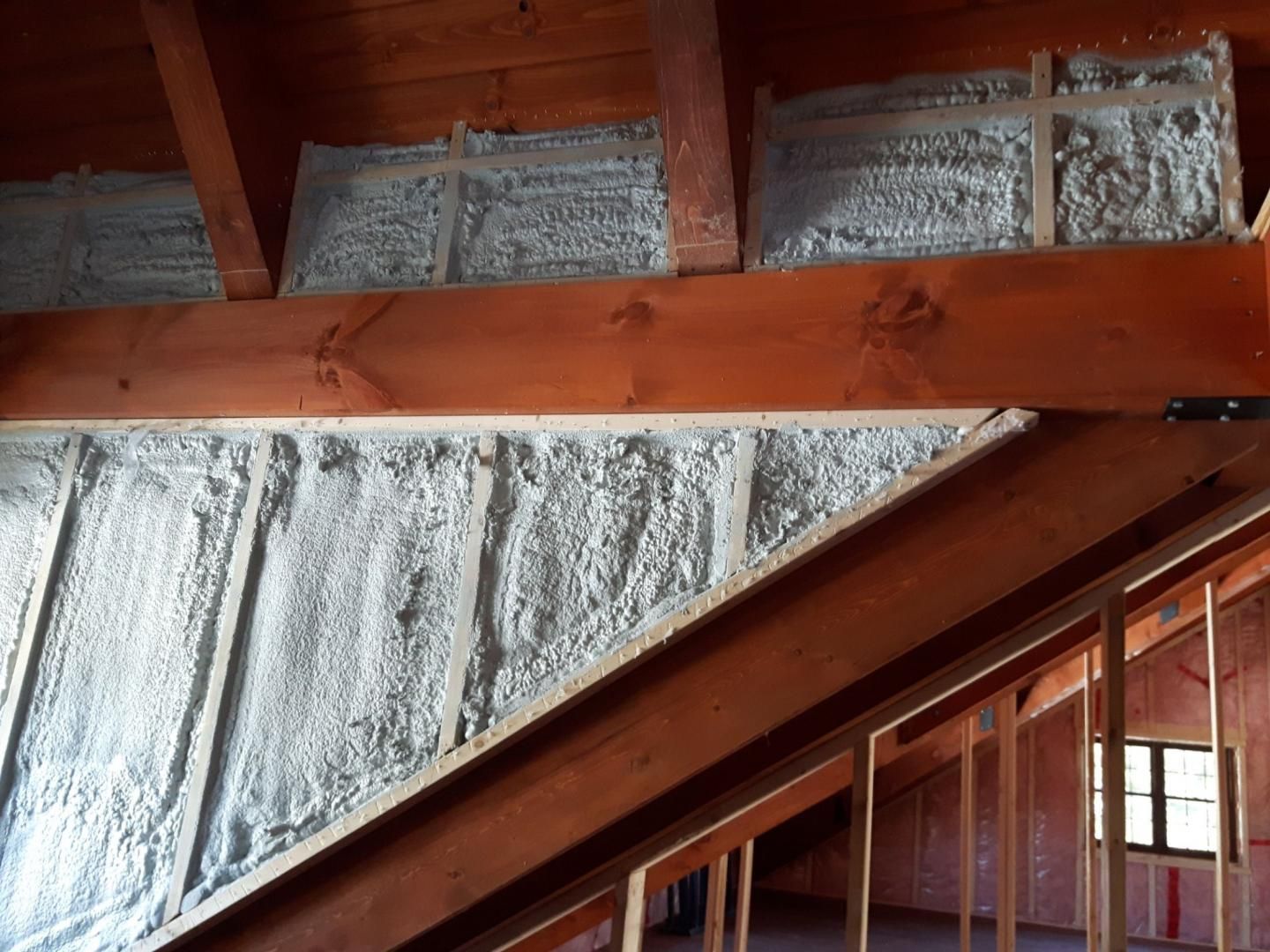 Grenier avec poutres en bois et isolation en mousse pulvérisée dans les murs et le plafond.