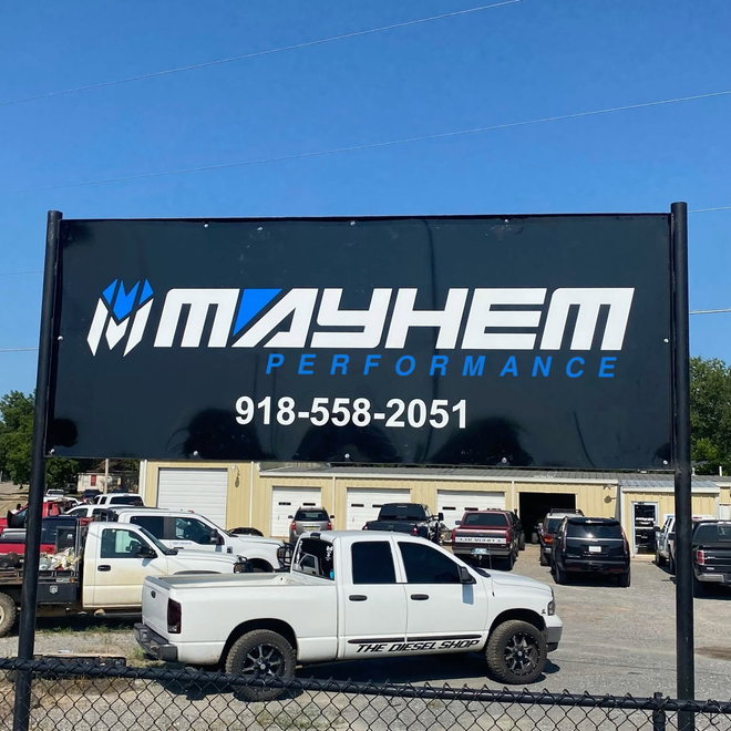 Mayhem Motors dealership sign with phone number above a white pickup truck