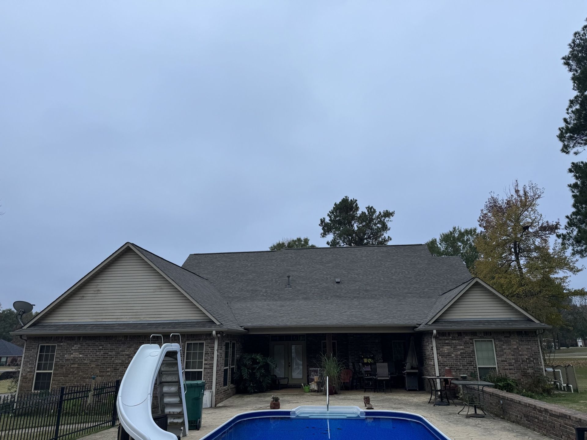 Backyard with house, pool, and slide under a cloudy sky.