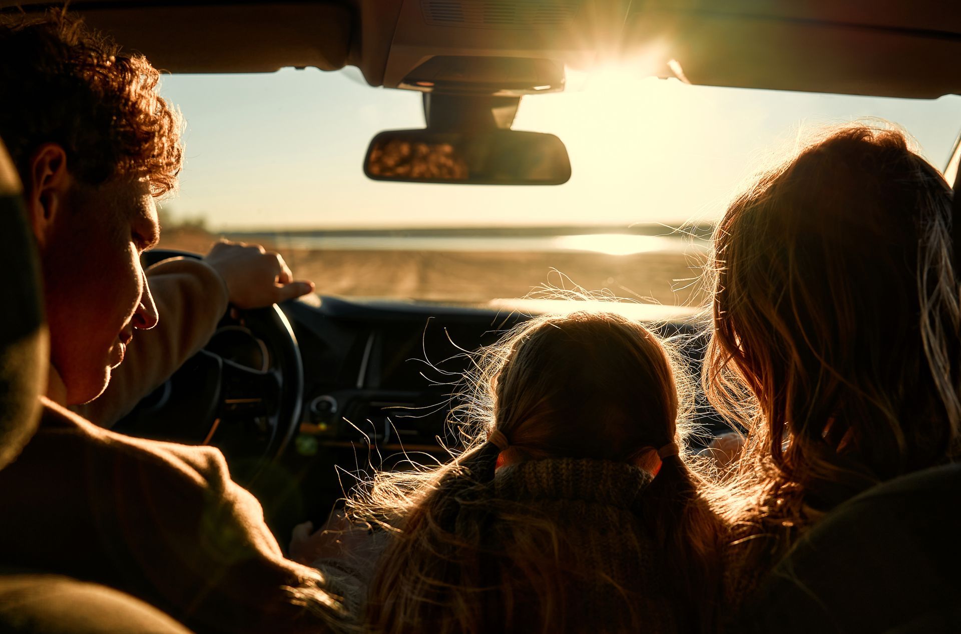 A man is driving a car with two children in the back seat.