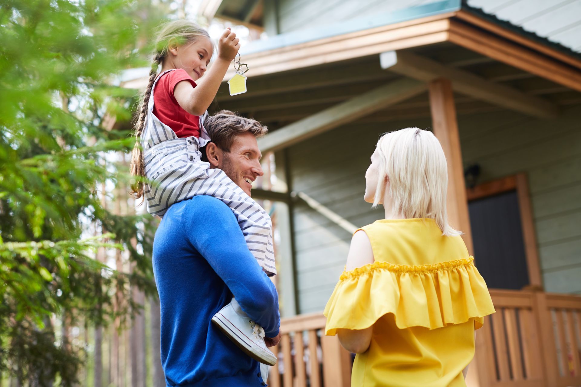 A man is carrying a little girl on his shoulders while a woman looks on.