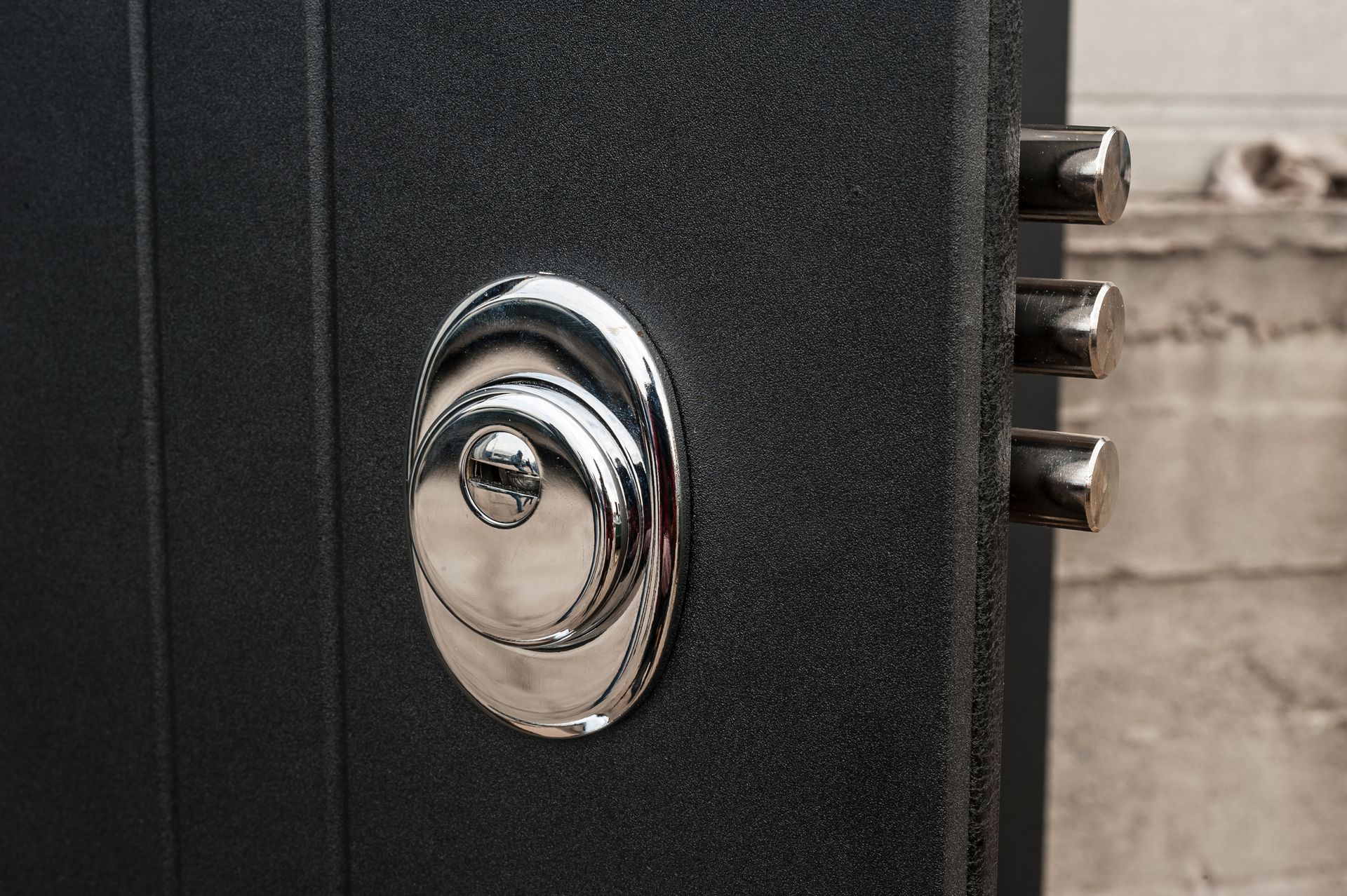 Primo piano di una porta scura con una serratura e dei catenacci color argento lucido.