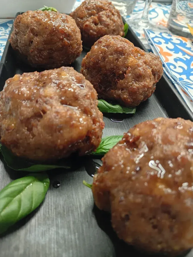 Polpette e foglie di basilico su un piatto rettangolare nero.