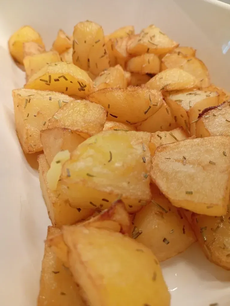 Spicchi di patate arrostite condite con erbe aromatiche in una ciotola bianca.