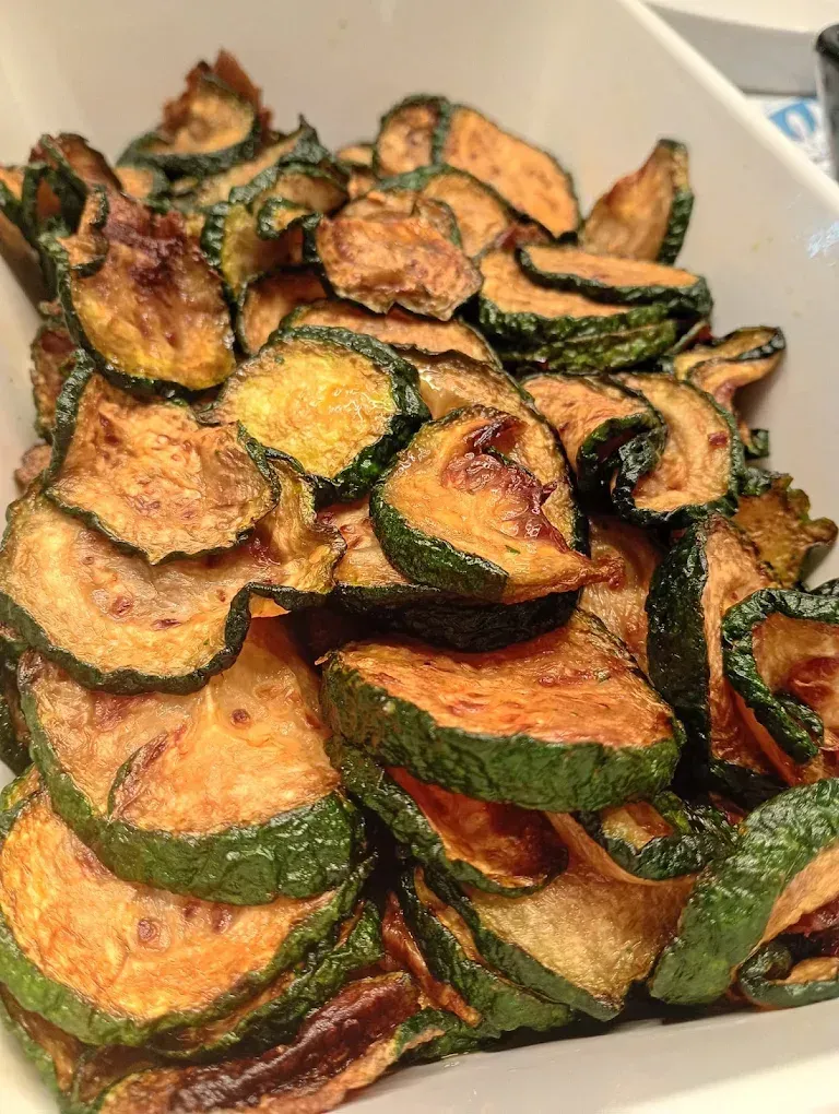 Mucchio di chips di zucchine croccanti e dorate in una ciotola bianca da portata.
