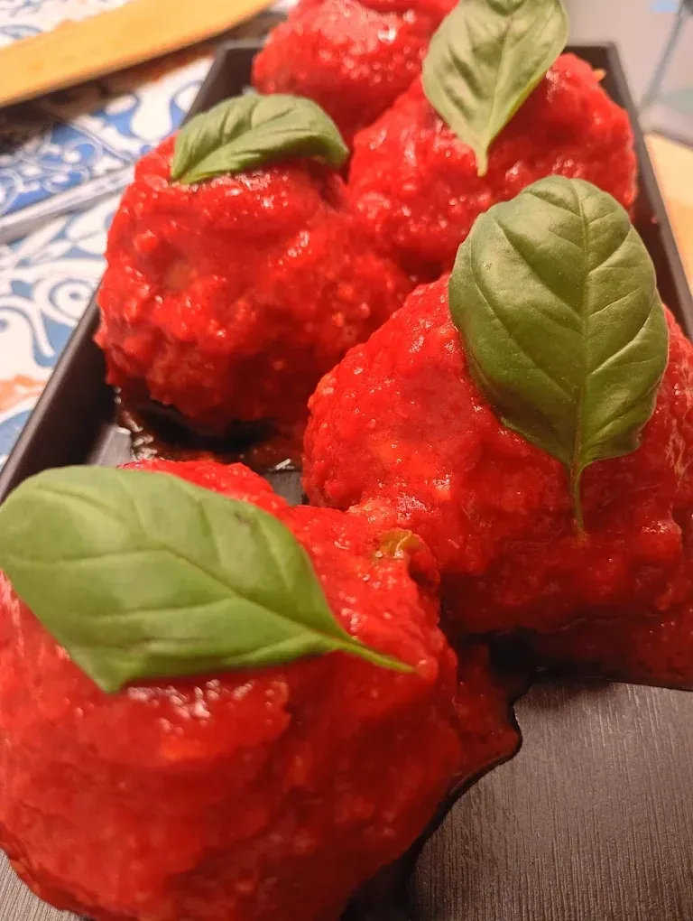Polpette in salsa di pomodoro, guarnite con foglie di basilico, su un vassoio nero.