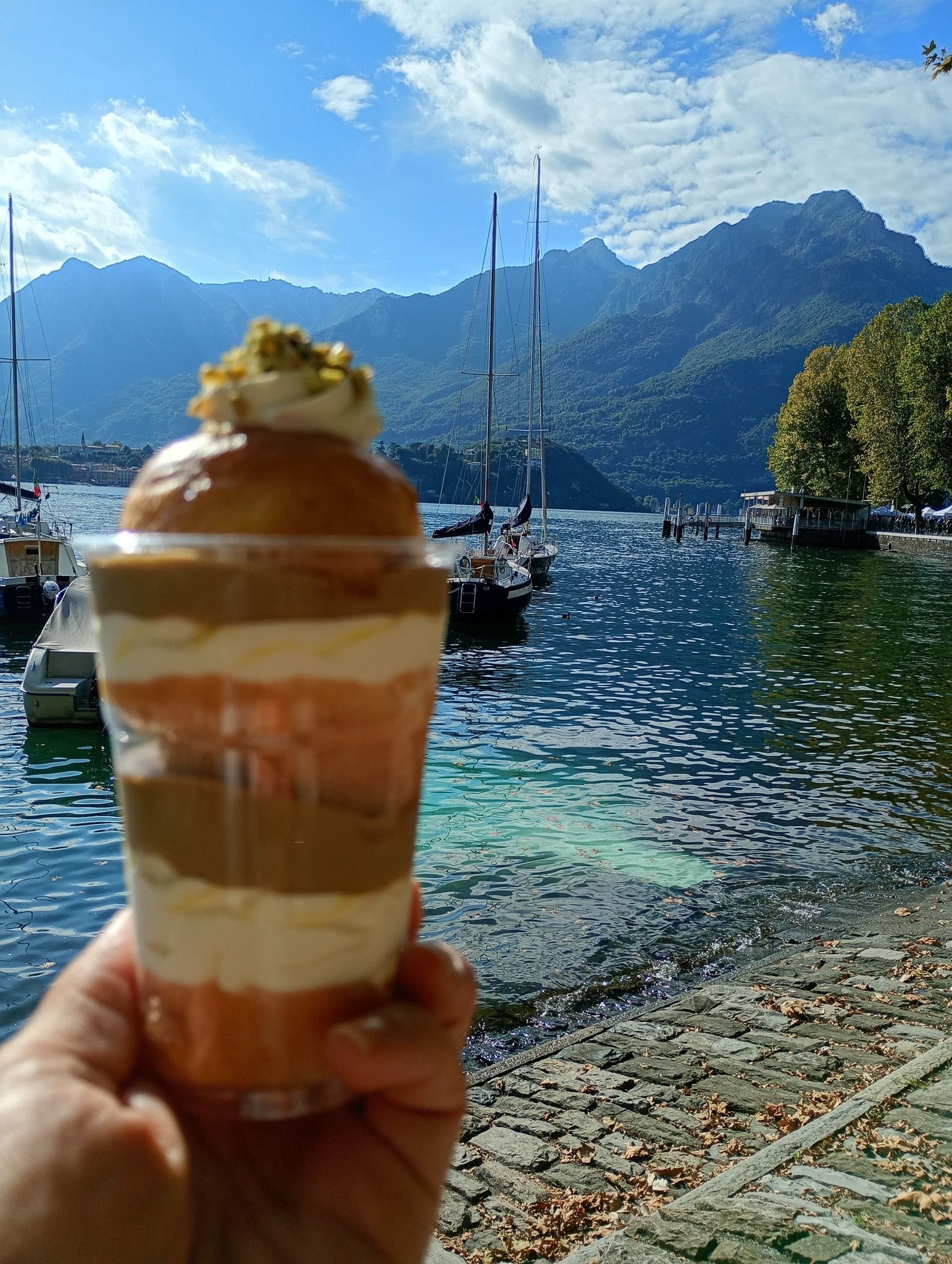 Mano che tiene un dessert a strati, lago e montagne sullo sfondo.