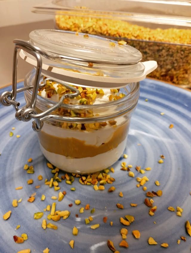 Barattolo di dessert con strati di crema, guarnito con pistacchi tritati.