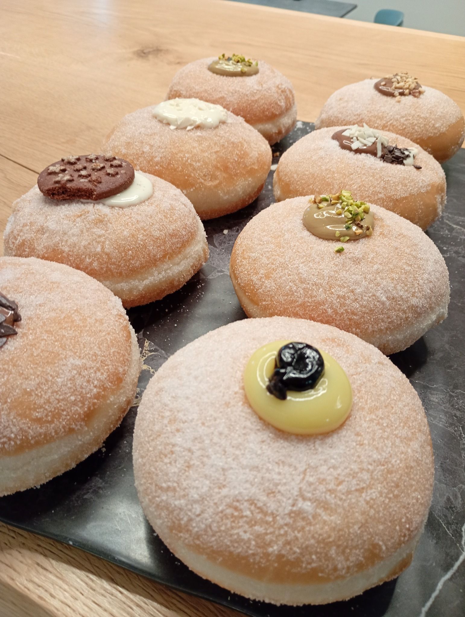 Primo piano di un vassoio di ciambelle ricoperte di zucchero a velo, ciascuna guarnita con una crema o un cioccolato diverso.