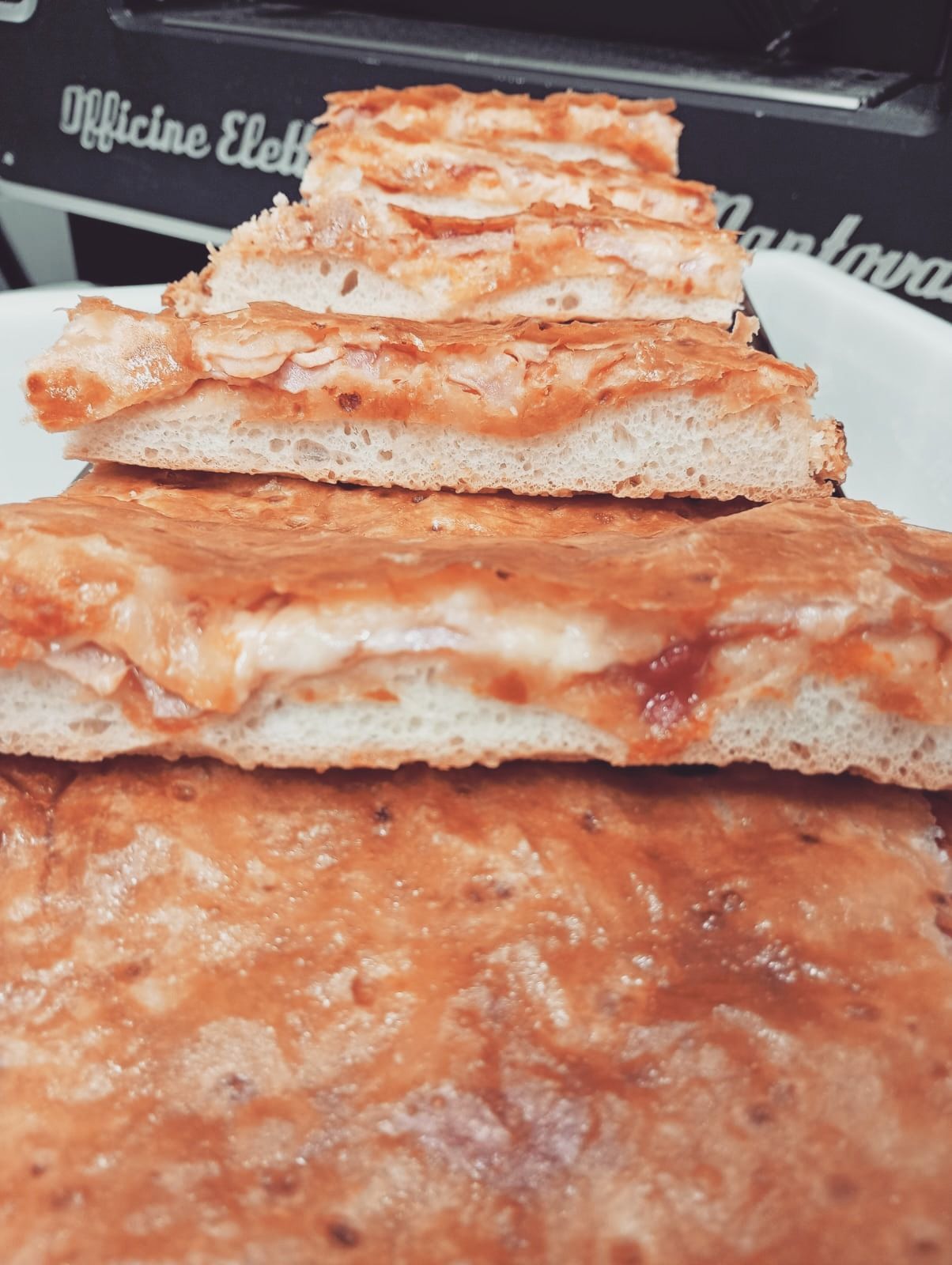 Primo piano di diverse fette quadrate di pizza margherita, impilate su un piatto bianco.