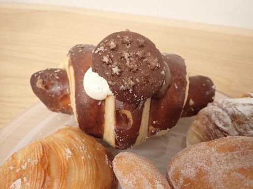 Primo piano di un croissant al cioccolato con un ciuffo di panna, circondato da altri prodotti da forno.