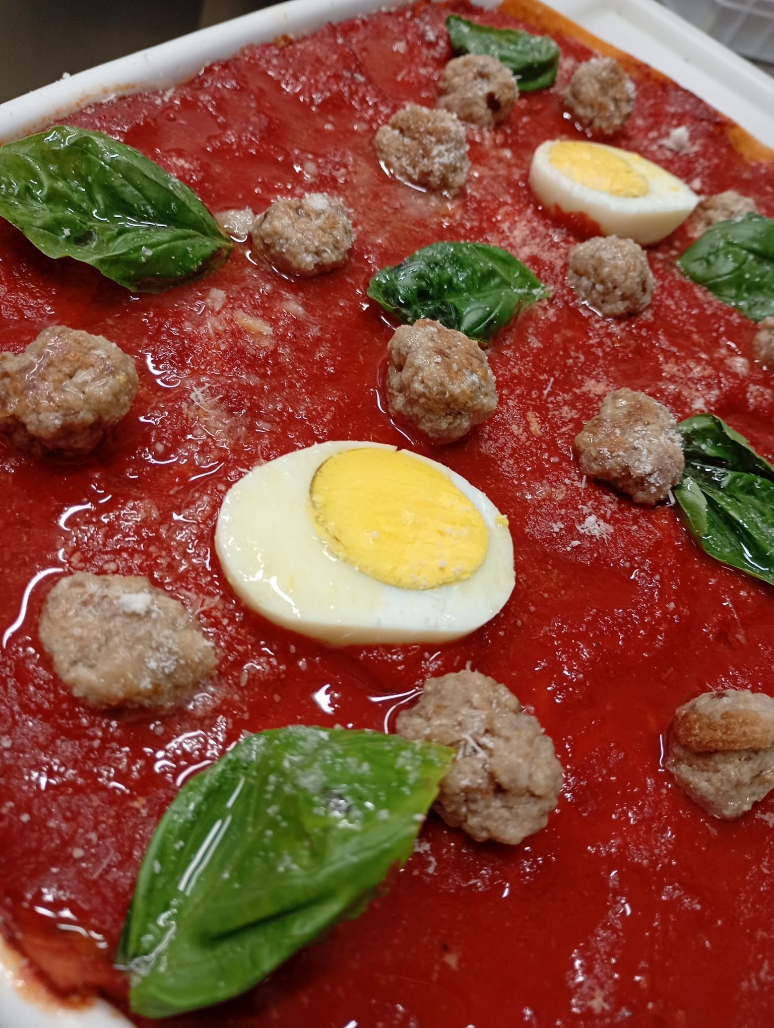 Piatto quadrato di salsa rossa con polpette, foglie di basilico e uova sode tagliate a fette.