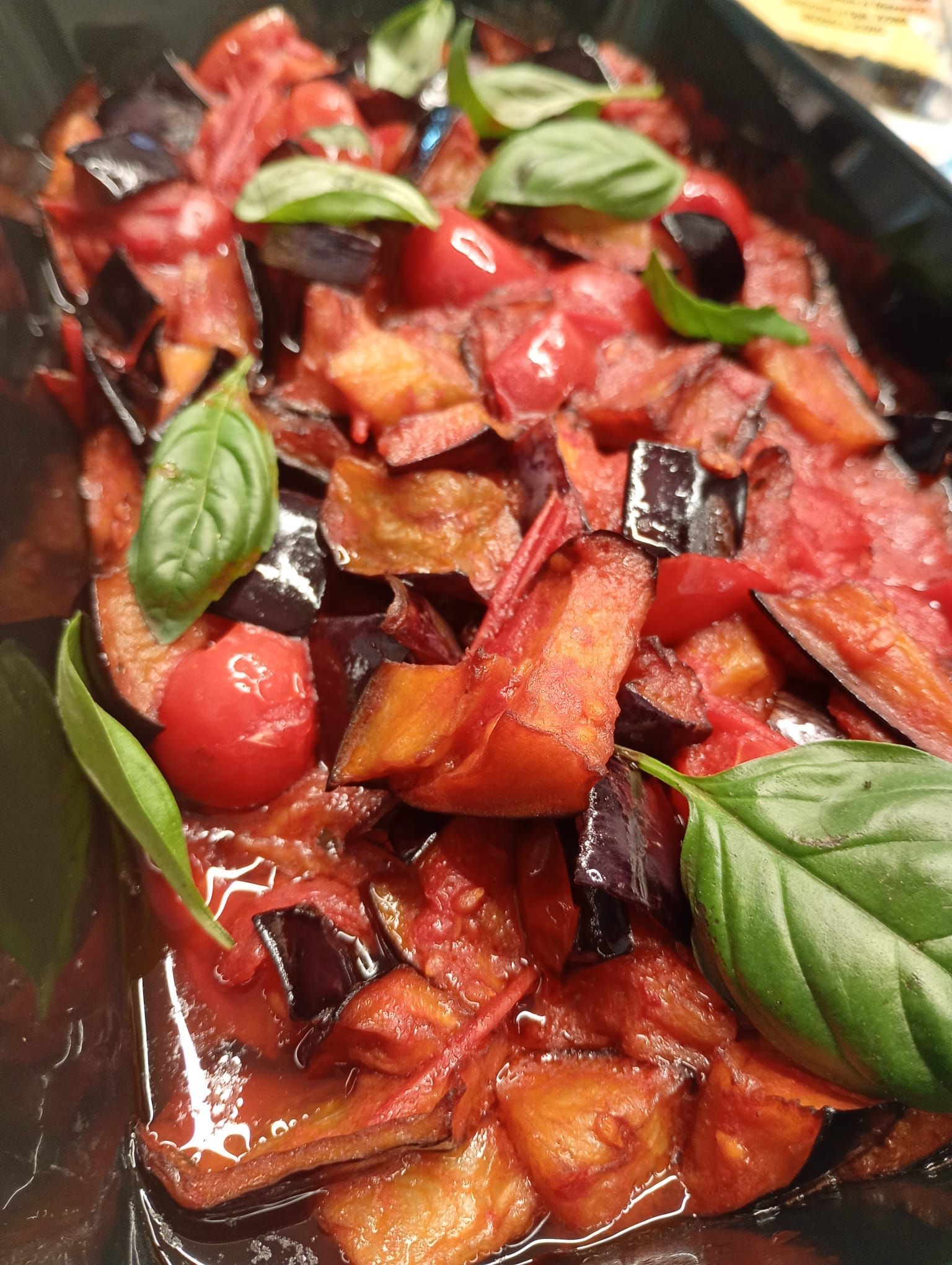 Melanzane e pomodori in un vassoio, guarnito con basilico fresco.